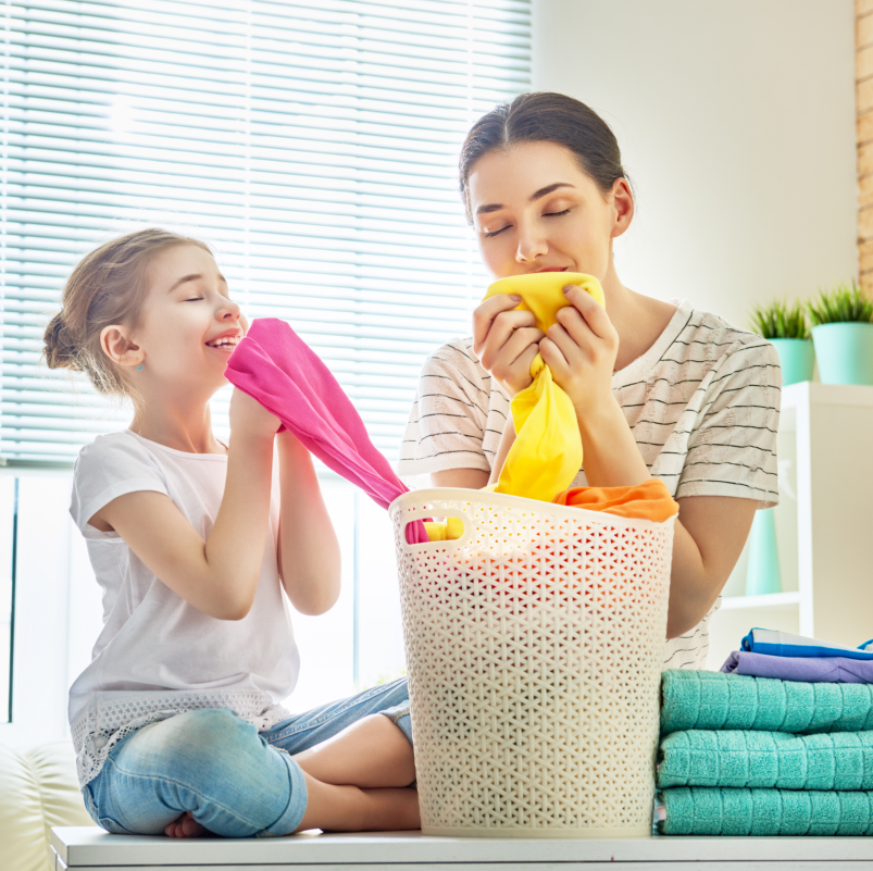 Mother and daughter cheerfully fold bright laundry into a white basket.
